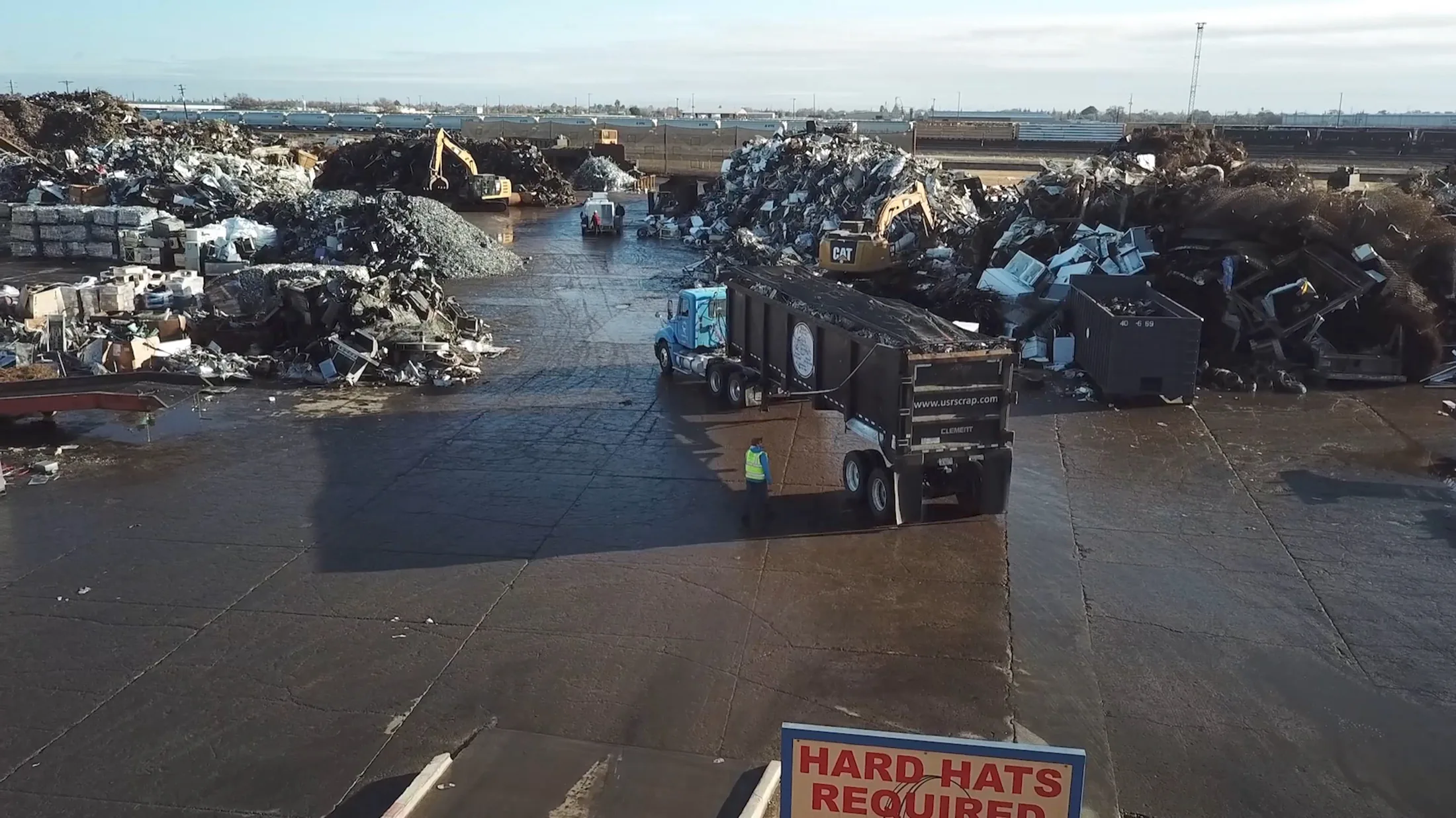 Real recycling yard reference showing trucks, machines and multiple material piles.